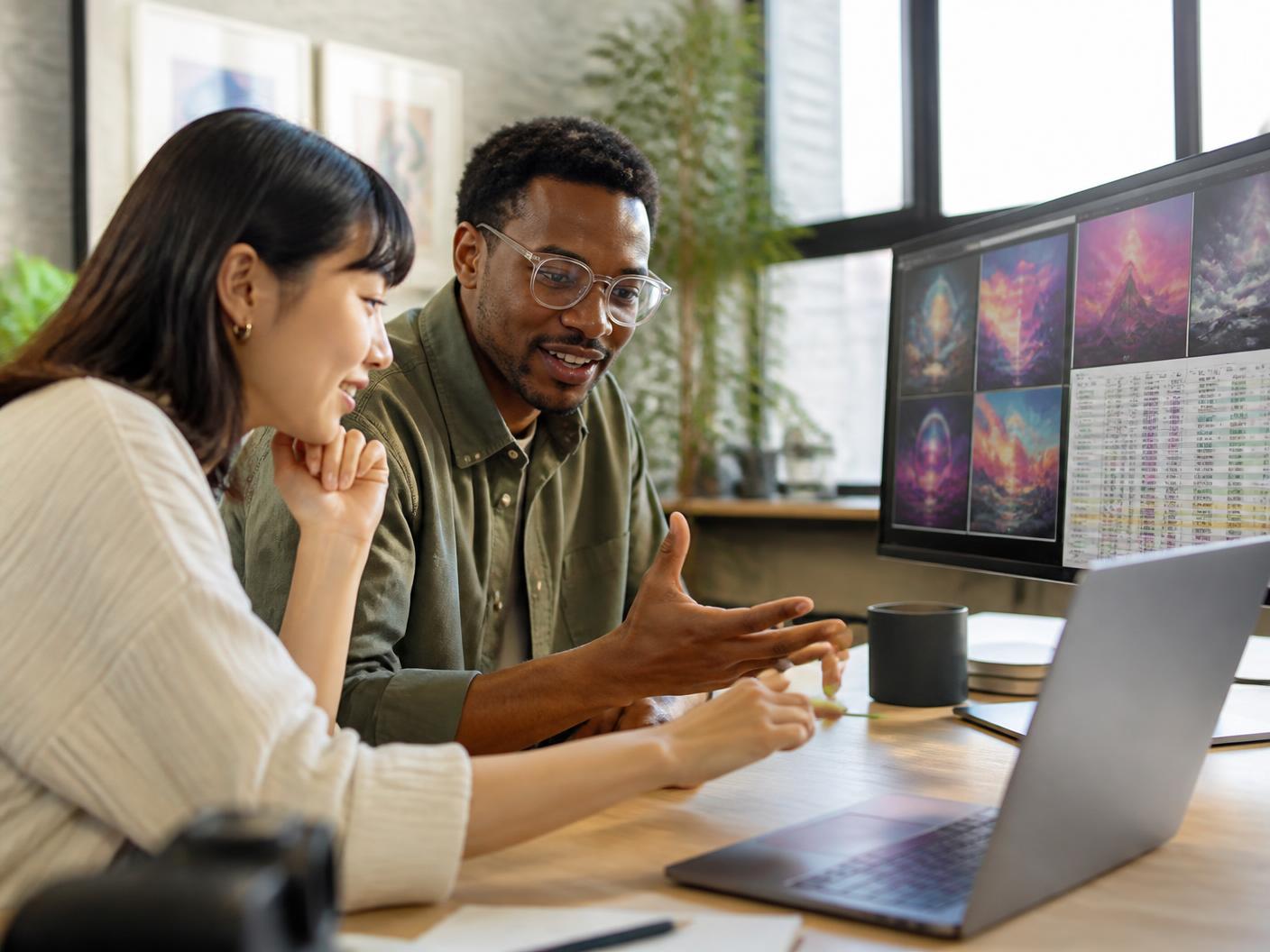 Two young professionals building a generative AI tool on a laptop beside a monitor of generated images and structured data